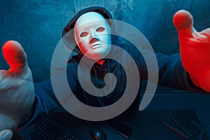 Anonymous hacker wearing face mask working on computer in dark room
