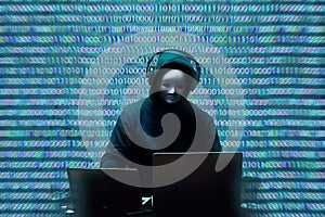 Anonymous hacker wearing face mask working on computer in dark room