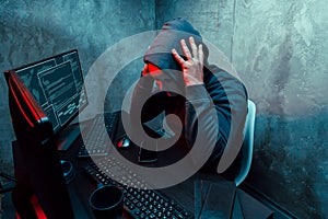 Anonymous internet hacker with mask sitting at the table and using computer