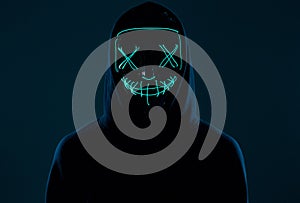 Anonymous man in black hoodie hiding his face behind a neon mask