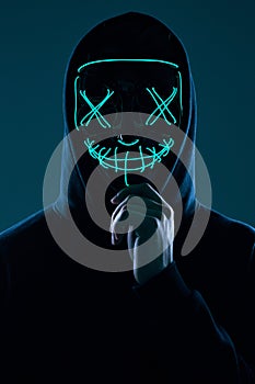 Anonymous man in black hoodie hiding his face behind a neon mask