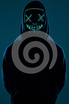 Anonymous man in black hoodie hiding his face behind a neon mask