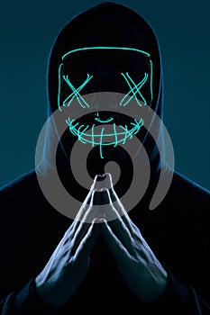 Anonymous man in black hoodie hiding his face behind a neon mask