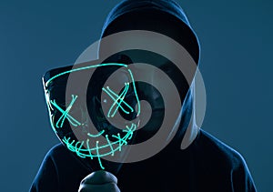 Anonymous man in black hoodie hiding his face behind a neon mask