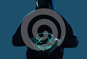 Anonymous man in black hoodie hiding his face behind a neon mask