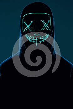 Anonymous man in black hoodie hiding his face behind a neon mask