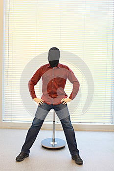 Anonymous man in black sack on head sitting on pneumatic stool