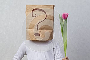 An anonymous man with a box on his head that limits his identity holds a flower