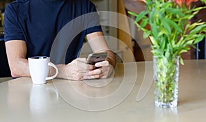 Anonymous man with cellphone on table and coffee cup and flower vase