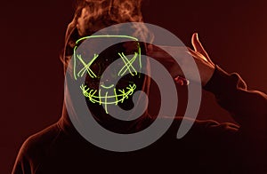 Anonymous man hiding his face behind neon mask in a colored smoke