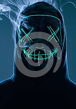 Anonymous man hiding his face behind neon mask in a colored smoke