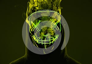 Anonymous man hiding his face behind neon mask in a colored smoke