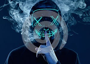 Anonymous man hiding his face behind neon mask in a colored smoke