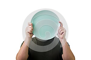 Anonymous man hiding his identity, covering face using an empty dish plate. Global crisis and hunger issue. Food supply problem.