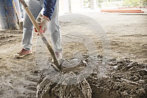 An anonymous man mixes a batch of concrete with a shovel. Manual construction labor.