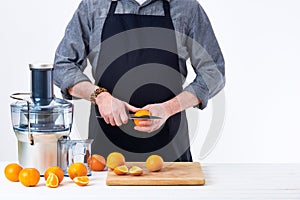 Anonymous man preparing fresh orange juice using electric juicer, healthy lifestyle detox concept on white background.