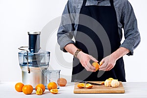 Anonymous man preparing fresh orange juice using electric juicer, healthy lifestyle detox concept.