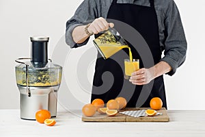 Anonymous man wearing an apron, pouring freshly prepared orange juice into a glass, healthy lifestyle concep