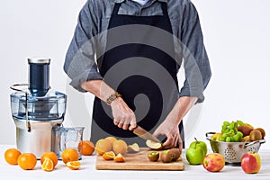 Anonymous man wearing an apron, preparing fresh fruit juice using modern electric juicer, healthy lifestyle detox concept on white