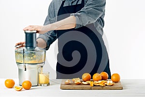 Anonymous man wearing an apron, preparing healthy orange juice, using modern electric juicer, healthy lifestyle concept