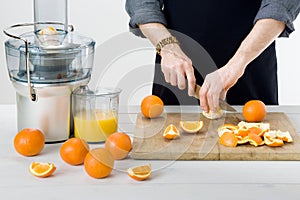 Anonymous man wearing an apron, preparing healthy orange juice, using modern electric juicer, healthy lifestyle concept