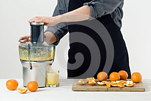 Anonymous man wearing an apron, preparing healthy orange juice, using modern electric juicer, healthy lifestyle concept