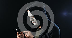 Anonymous masked fraudster in hood demands a ransom for blackmail using a smartphone. Masked Criminal intimidates the