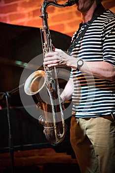 An anonymous musician in a striped t-shirt plays the saxophone in a jazz bar, live performance