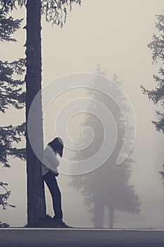 Anonymous woman leaning against tree