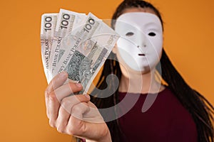 An anonymous woman stands and pulls her hand in with paper banknotes with the face value of one hundred Polish zlotys