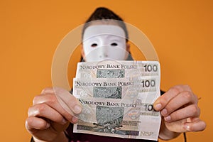 An anonymous woman stands and pulls her hand in with paper banknotes with the face value of one hundred Polish zlotys