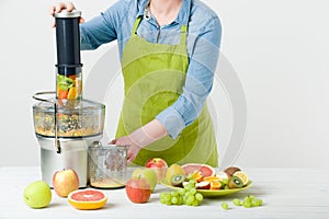 Anonymous woman wearing an apron, preparing healthy fruit juice using modern electric juicer, healthy lifestyle concept