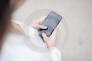 An anonymous young woman fidgeting with her phone or playing a game while walking at the sidewalk. Blank screen for editing