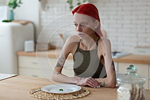 Anorexic woman looking awful sitting near plate with three peas