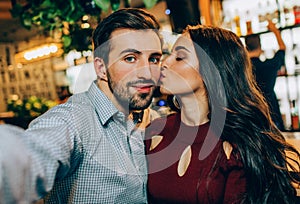 Another selfie of couple. Girl is kissing her partner while he is taking a picture. They look happy together.