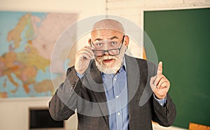 answer and question. senior man teacher at blackboard. bearded tutor in glasses near geography map. back to school