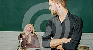 Answering home assignment. Male student with examiner at examination. Handsome man standing hands crossed in classroom