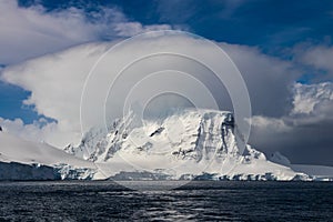 Antarctic mountain; cloud on top of peak; ocean in foreground.