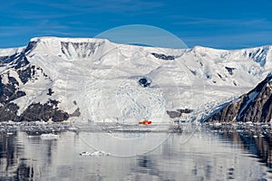 Antarctic seascape with icebergs, reflection and orange ship