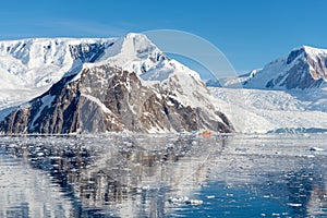 Antarctic seascape with icebergs, reflection and orange ship