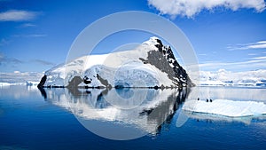 Antarctica, Lemaire Channel, snow covered mountain reflecting in sea. Penguins on ice floe in beautiful landscape.