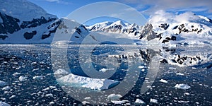 Antarctica, panoramic scenery with snowcapped mountains reflecting in blue water with ice flows, Lemaire Channel near Paradise Bay