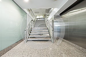 An antechamber with glass and stainless steel walls and stairs going up with metal railings and pink granite steps