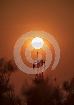 The antenna for telecommunications and big sunset background is silhouette and heat weather