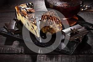 Anthill cake and cheese cake with chocolate and condensed milk next to cup of tea on a wooden table. Low key.