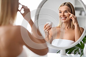 Anti-Age Skincare. Beautiful Middle Aged Woman Applying Moisturising Eye Cream Near Mirror
