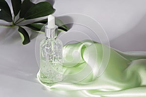 Anti aging serum with collagen and peptides in glass bottle with dropper on a gray background with green leaves