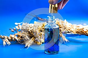 Anti aging serum in glass bottle with dropper on blue background and dry flowers . Facial liquid serum with collagen and peptides photo