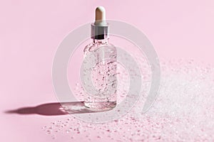 Anti aging serum in a glass bottle on a pink background with snow.