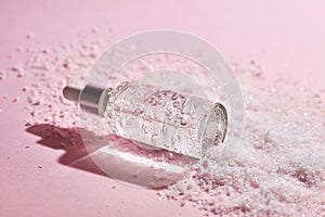 Anti aging serum in a glass bottle on a pink background with snow.